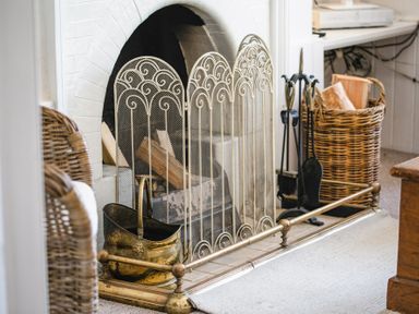 A fireplace with a decorative screen a brass coal bucket and a wicker basket with firewood at Elliot Cottage in Bamburgh