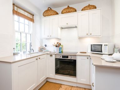A kitchen with white cabinets a window a microwave an oven and utensil holder at Elliot Cottage in Bamburgh