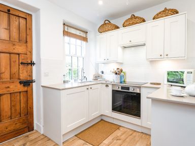 A kitchen with white cabinets a wooden door a window and kitchen appliances at Elliot Cottage in Bamburgh