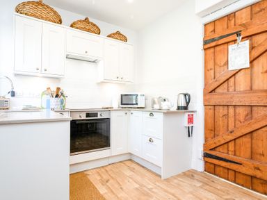 A kitchen with white cabinets a microwave kettle oven and wooden door at Elliot Cottage in Bamburgh
