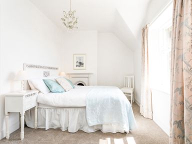 A bedroom with a bed lamps a chair curtains and a framed picture at Elliot Cottage in Bamburgh