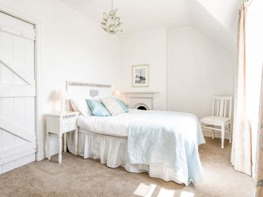 A bedroom with a bed pillows bedside tables lamps a chair and a framed picture at Elliot Cottage in Bamburgh