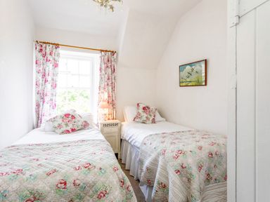 A bedroom with two single beds floral bedspreads and pillows a nightstand with lamp floral curtains and a painting on the wall at Elliot Cottage in Bamburgh