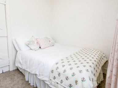 A bed with white bedspread and floral pillows in a corner bedroom at Elliot Cottage in Bamburgh