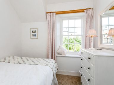 A bedroom with a bed next to a window with curtains a white dresser with a lamp and a mirror at Elliot Cottage in Bamburgh