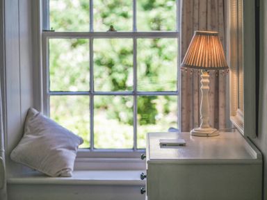 A window with a pillow on the sill and a table with a lamp and a small object at Elliot Cottage in Bamburgh