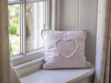A cushion with a heart design on a window sill next to floral curtains at Elliot Cottage in Bamburgh