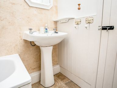 A bathroom with a pedestal sink and two towel hooks on the wall at Elliot Cottage in Bamburgh