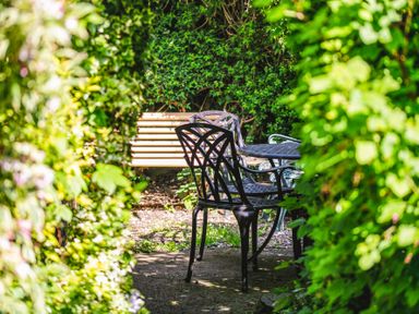 A garden seating area with a metal table and chairs and a wooden bench surrounded by greenery at Elliot Cottage in Bamburgh