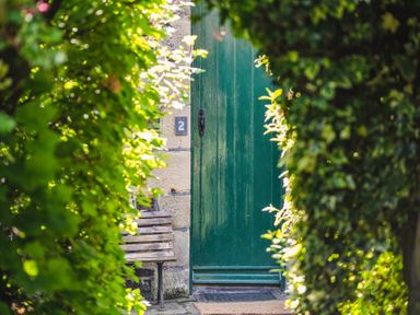 A green wooden door with a number 2 plaque and a wooden bench beside it surrounded by green foliage at Elliot Cottage in Bamburgh