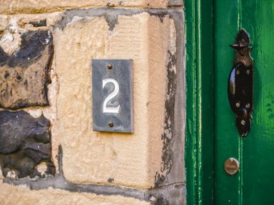 A house number 2 plate on a stone wall next to a green door with a black handle
