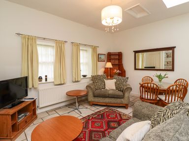 A living room with two sofas a television on a wooden stand and a dining table with four chairs at Glebe Cottage in Bamburgh