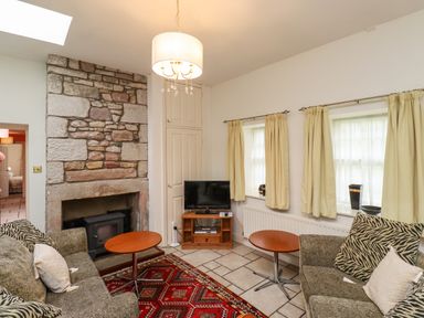 A living room with two sofas a red patterned rug a stone fireplace a small television and cream curtains at Glebe Cottage in Bamburgh