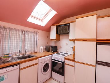 A kitchen with a washing machine oven microwave and sink under a skylight at Glebe Cottage in Bamburgh