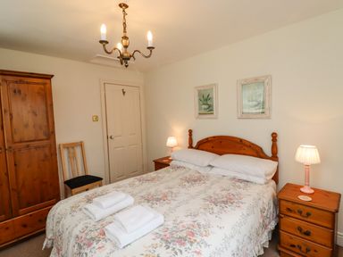 A bedroom with a double bed floral bedspread wooden wardrobe two bedside tables with lamps and framed pictures on the wall at Glebe Cottage in Bamburgh