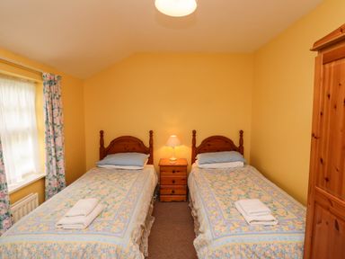 A bedroom with two single beds a wooden nightstand with a lamp and a wooden wardrobe at Glebe Cottage in Bamburgh