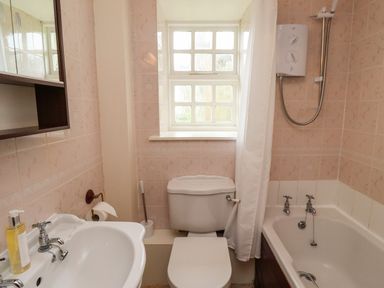 A bathroom with a sink a toilet a bathtub with shower and a window at Glebe Cottage in Bamburgh