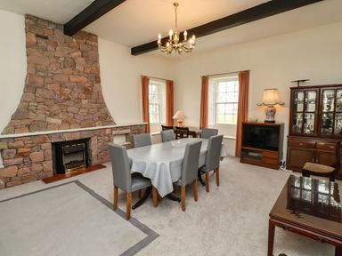 A dining room with a stone fireplace a table with six chairs and a cabinet at Glebe House in Bamburgh