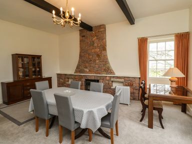 A dining room with a dining table covered by a polka dot tablecloth and six chairs a stone fireplace a wooden cabinet a small table with two chairs and a lamp at Glebe House in Bamburgh