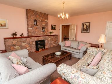A living room with sofas around a wooden coffee table and a stone fireplace at Glebe House in Bamburgh