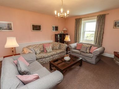 A living room with three sofas a coffee table lamps and framed pictures on walls at Glebe House Bamburgh