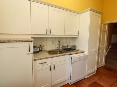 A kitchen with white cabinets a stainless steel sink dish drainer and a dishwasher at Glebe House in Bamburgh