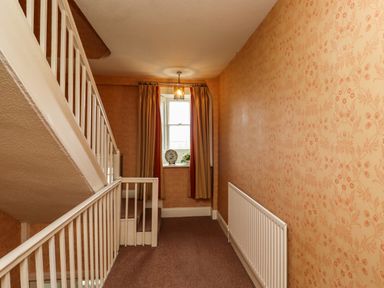 A hallway with staircase and a window with curtains and a radiator on the wall at Glebe House in Bamburgh