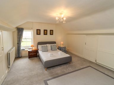 A bedroom with a gray bed and blue checkered cushions and curtains at Glebe House in Bamburgh