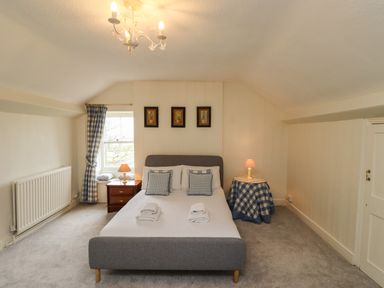 A bedroom with a grey bed two bedside tables with lamps checked curtains three framed pictures on the wall at Glebe House in Bamburgh
