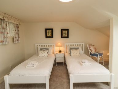 A bedroom with two single beds a nightstand with a lamp and a wicker chair at Glebe House in Bamburgh