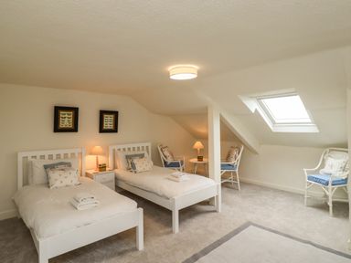 A bedroom with two single beds, chairs, lamps, and a skylight window at Glebe House in Bamburgh