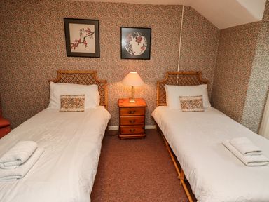 A bedroom with two single beds a wooden nightstand with a lamp and floral wallpaper at Glebe House Bamburgh