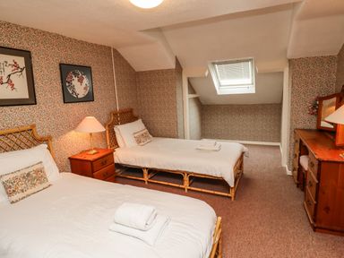 A bedroom with two single beds, a wooden nightstand with a lamp, floral wallpaper, and a wooden dresser with a mirror at Glebe House Bamburgh
