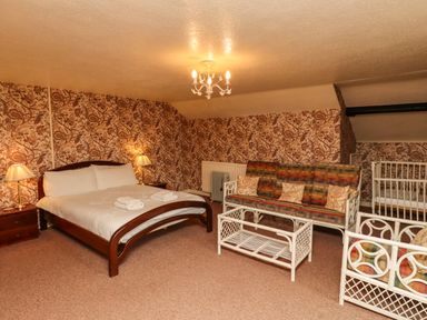 A bedroom with a double bed two bedside tables with lamps a sofa armchair coffee table and a baby crib at Glebe House in Bamburgh