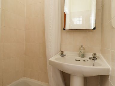 A bathroom corner with a sink a mirror shower curtain and tiled walls at Glebe House Bamburgh