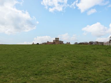 A grassy field with a castle and some buildings in the distance under a partly cloudy sky at Glebe House in Bamburgh