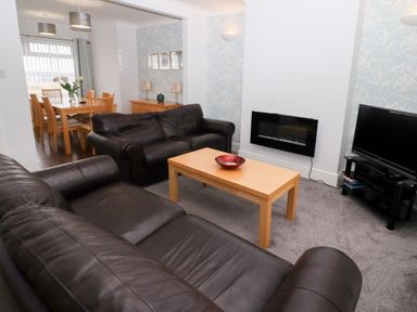 A living room with black leather sofas a wooden coffee table and a dining area at Bay View in Amble