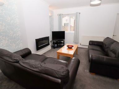 A living room with two black leather sofas a wooden coffee table with a bowl a wall-mounted electric fireplace and a television on a stand at Bay View in Amble