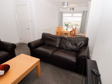 A living room with black leather sofas wooden coffee table and dining area with wooden chairs and table at Bay View in Amble