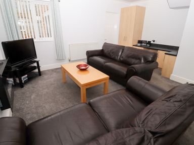 A living room with two brown leather sofas a wooden coffee table a flat screen television on a stand and a cabinet with countertop at Bay View in Amble