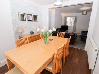 A dining room with a wooden table and chairs and a living room with sofas and a television at Bay View in Amble