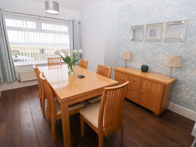 A dining room with a wooden table and chairs with flowers on the table and a sideboard with lamps at Bay View in Amble