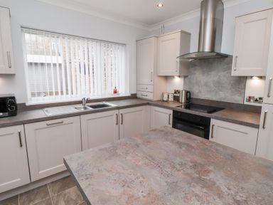 A kitchen with white cabinets a double sink a black microwave and stainless steel kettle at Bay View in Amble