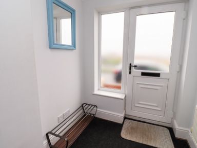 An entryway with a white door with frosted glass panels a small rectangular window a metal shoe rack a blue framed mirror and a doormat at Bay View in Amble