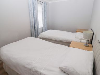 A bedroom with two single beds bedside tables and a window with curtains at Bay View in Amble