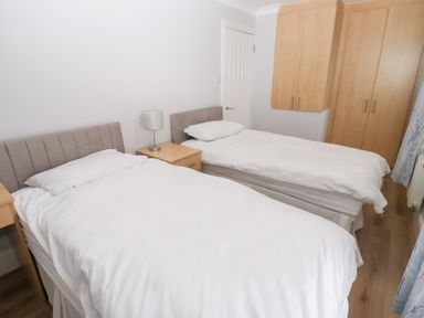 A bedroom with two single beds a nightstand with a lamp and built in wooden wardrobes at Bay View in Amble