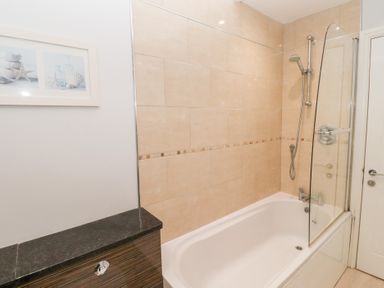 A bathroom with a bathtub shower combination beige tiled walls and a cabinet with a black countertop at Bay View in Amble