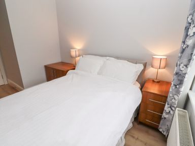 A bedroom with a white bed between two wooden nightstands with lamps at Bay View in Amble