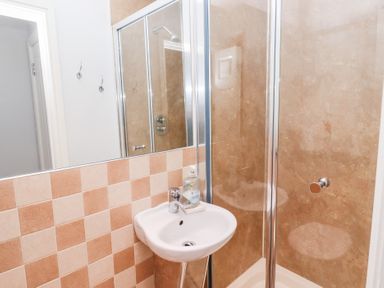 A bathroom with a small white sink with soap dispenser and a shower with glass door and beige tiles at Bay View in Amble