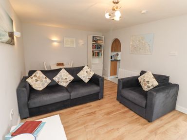 A living room with two sofas with patterned cushions a bookshelf a dining table and a map on the wall at Bedwine Cottage in Beadnell